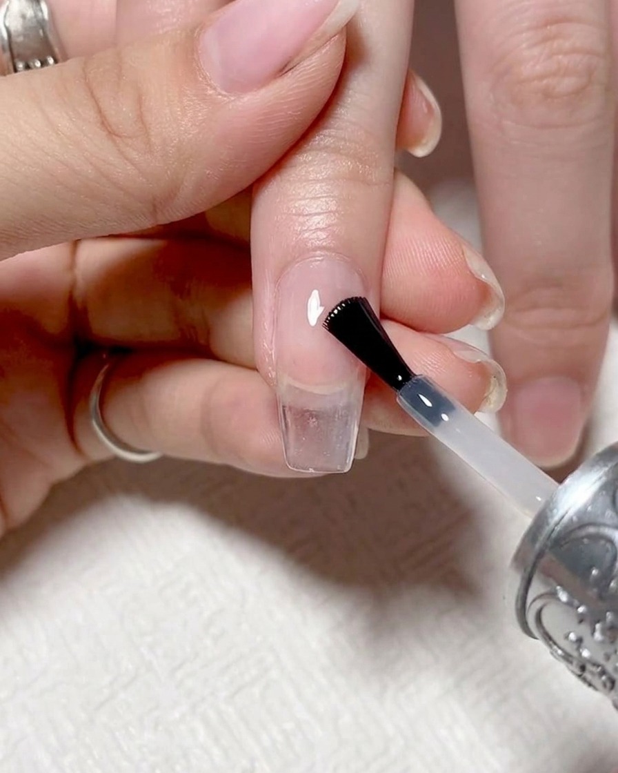 A close-up shot of a nail brush applying a clear, glossy top coat over a finished gradient nail.