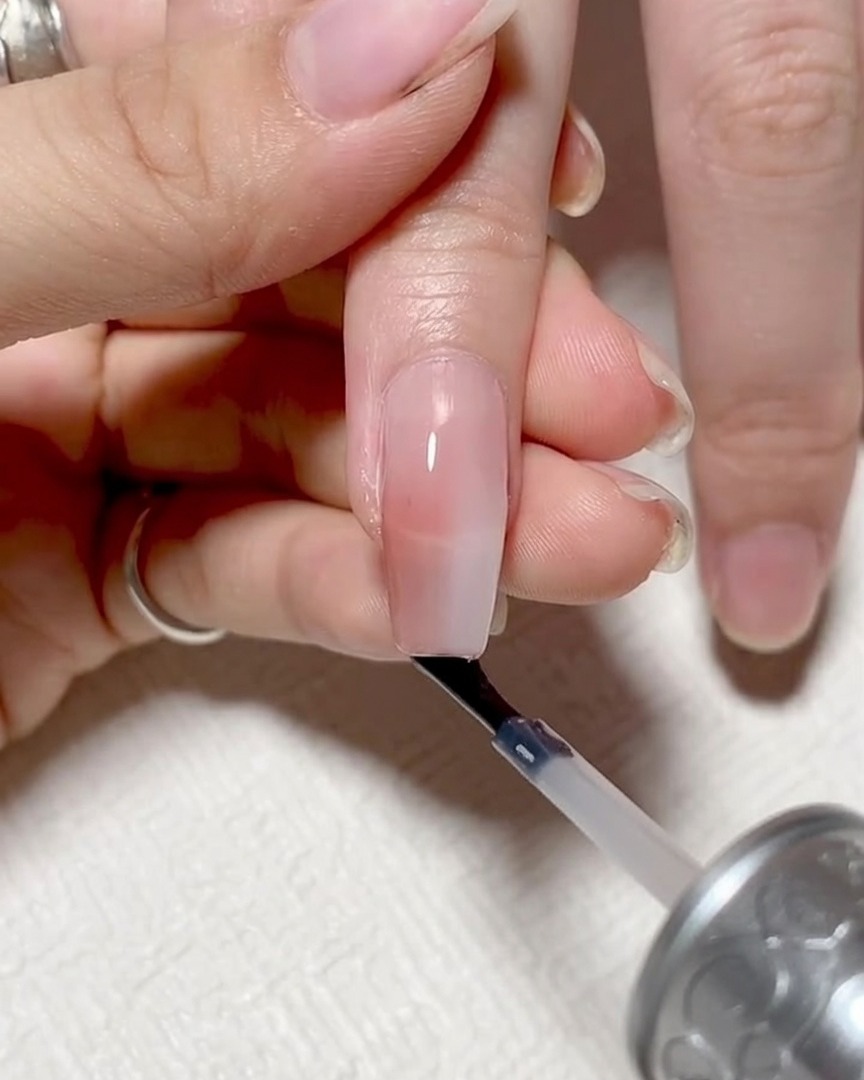 A close-up showing the nail brush horizontally running along the free edge of the nail to cap it.