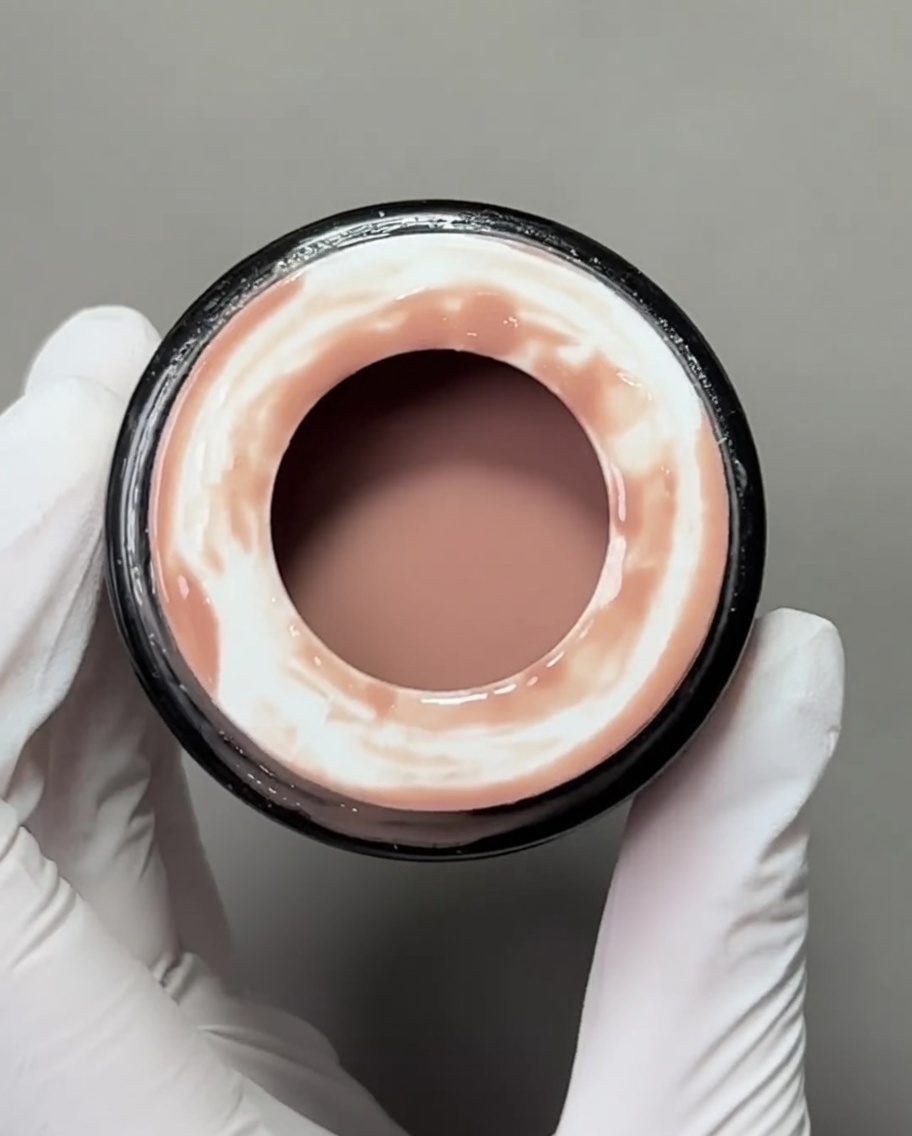 A close-up view of a flat gel brush applying a nude-colored base gel onto a nail tip.