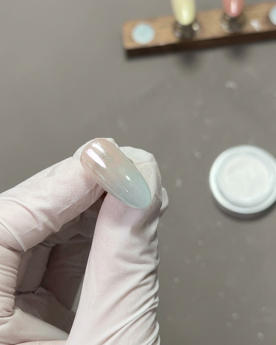 A close-up of a finger buffing the surface of a chrome-coated nail, creating a high-shine, mirror-like reflection.