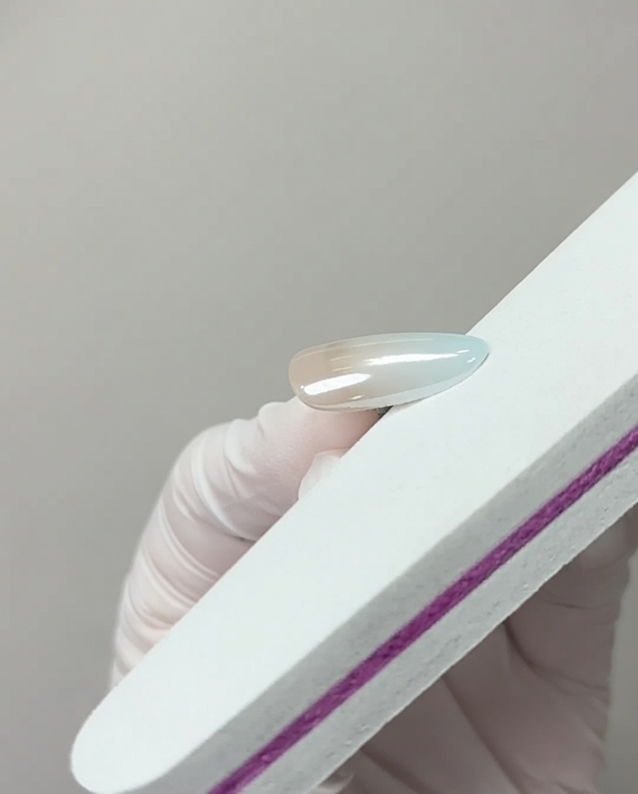 A nail file lightly touching the free edge of a chrome-finished nail to remove excess pigment.