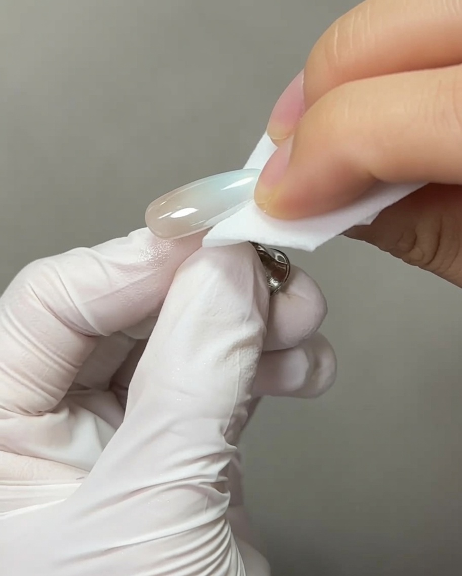 A close-up of a nail brush applying a clear bead of extension gel to the very tip of a chrome-finished nail.