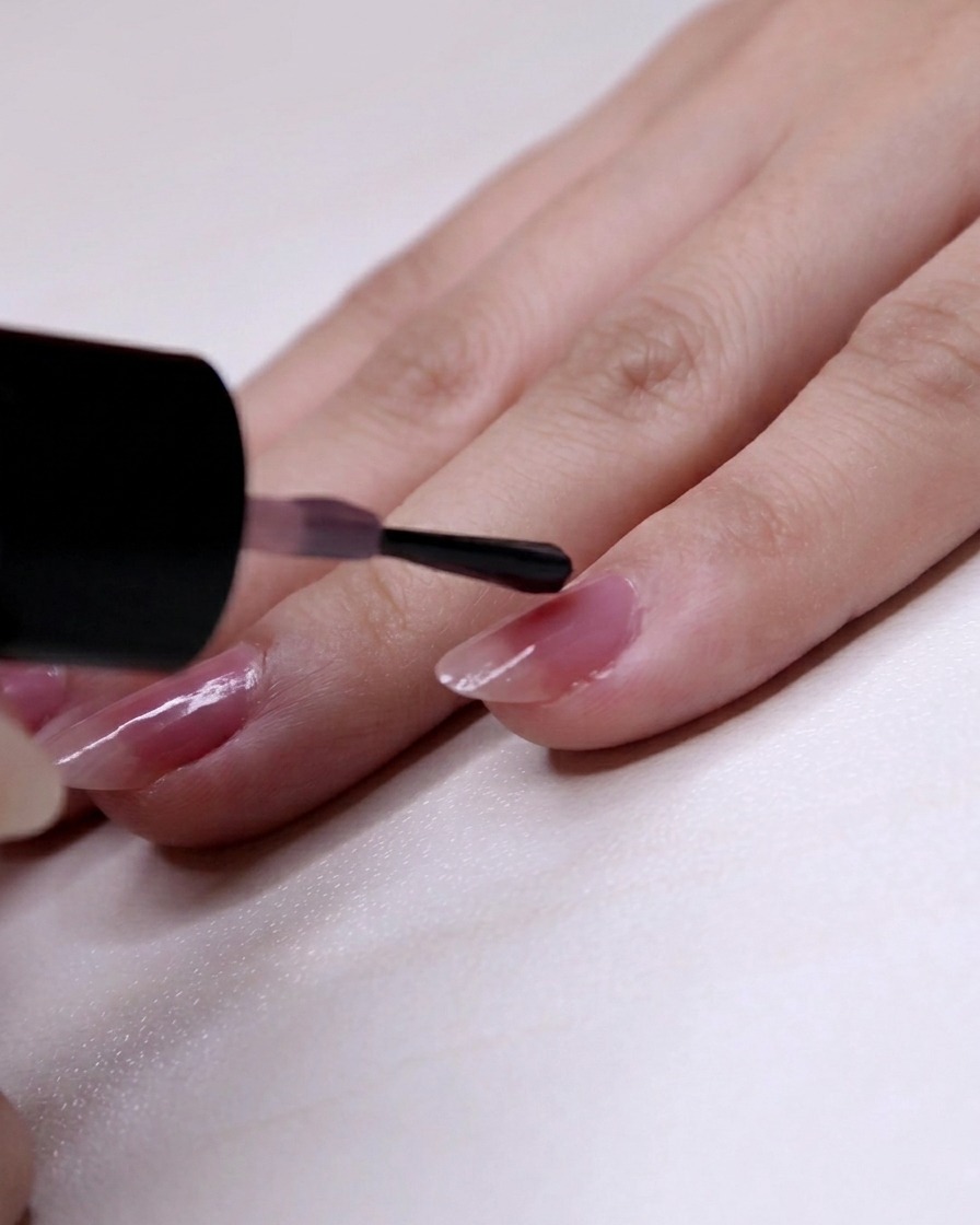 The pink polish being applied starting two-thirds from the cuticle down to the tip of the pinky nail.