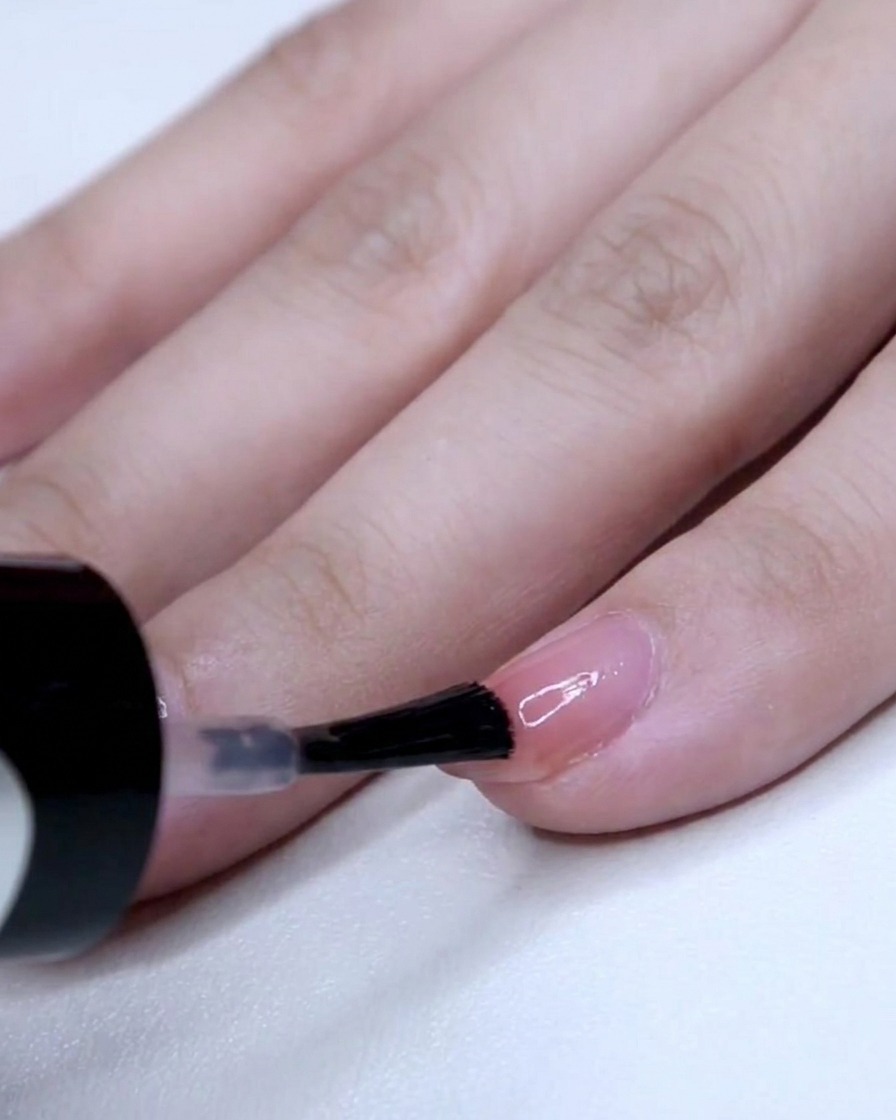 A nail brush applying a concentrated layer of pink polish to the tip of a pinky nail.