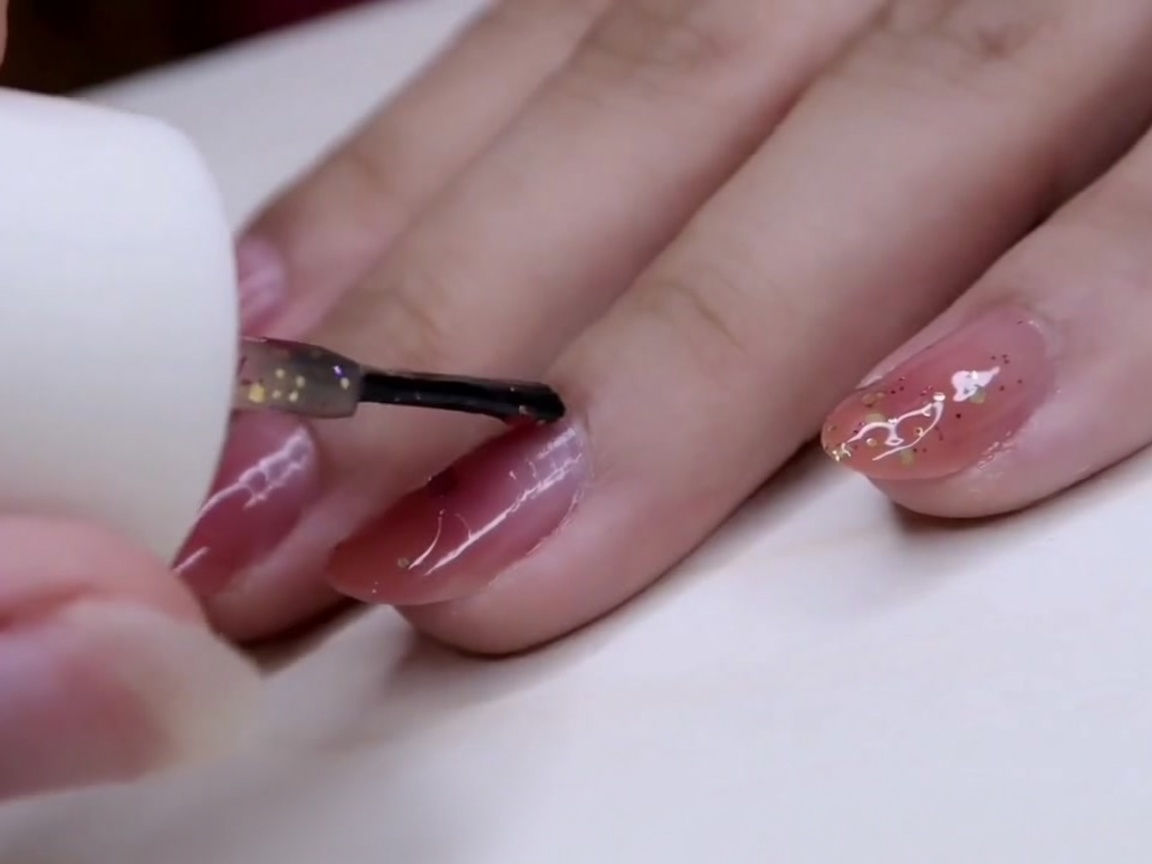 A brush spreading glitter polish over the middle finger, concentrating flakes near the tip.