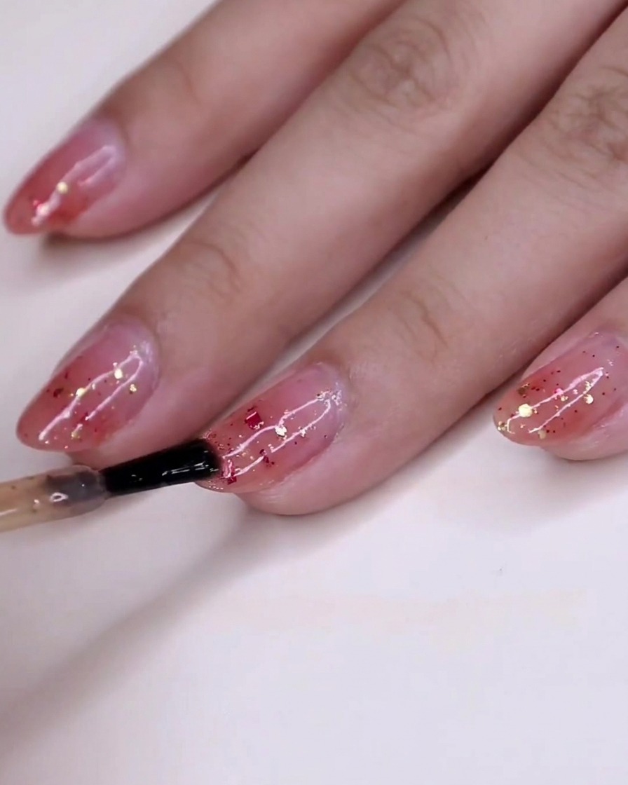 A view of the hand with wet glitter polish settling on the nails over the pink gradient base.