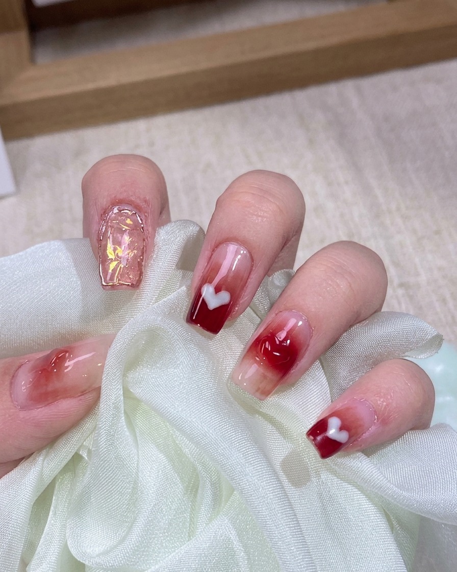 A fine detail brush applying sheer red jelly gel to the center of a prepped natural nail.