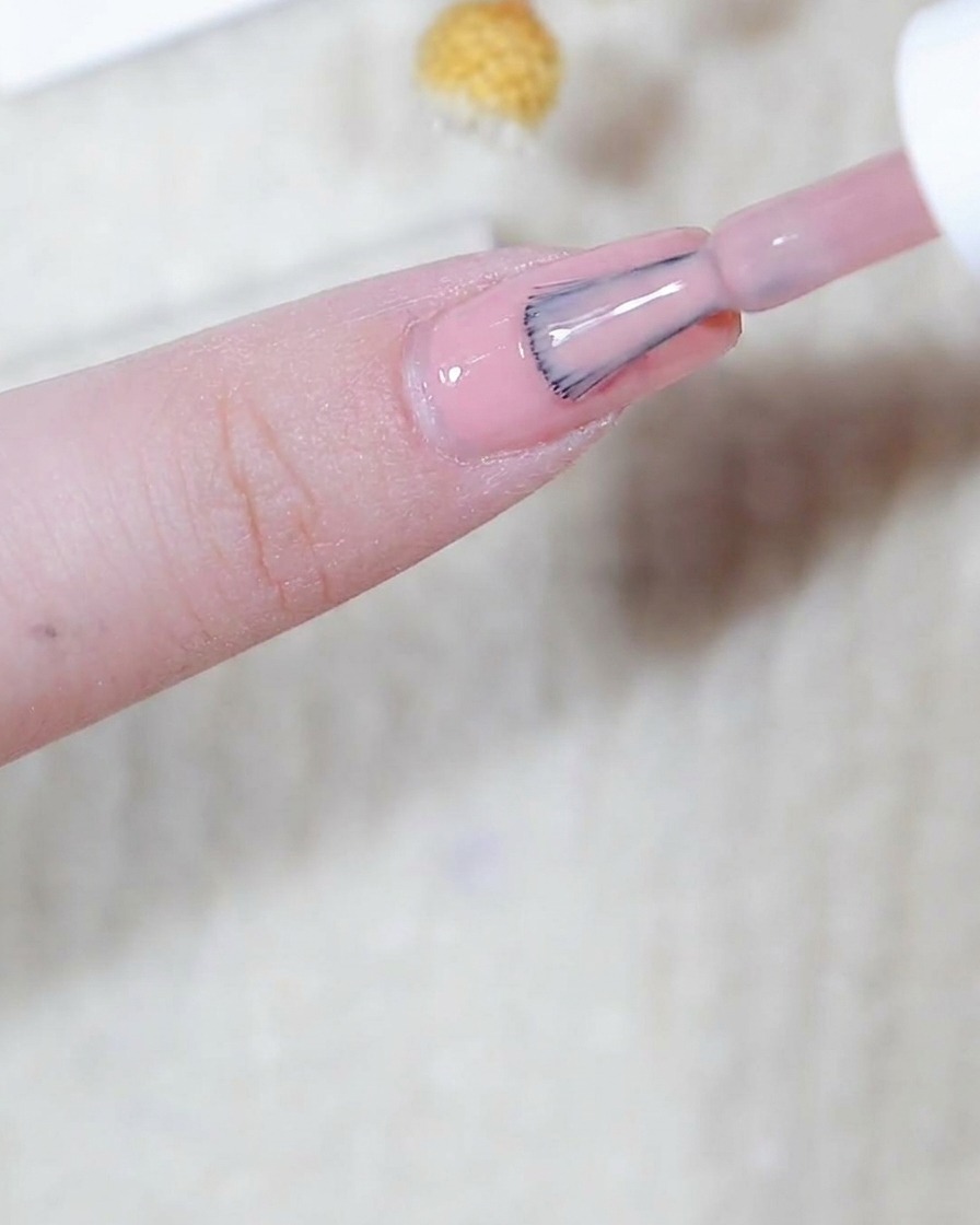 A brush applying a smooth, thin layer of pink base color to a fingernail.