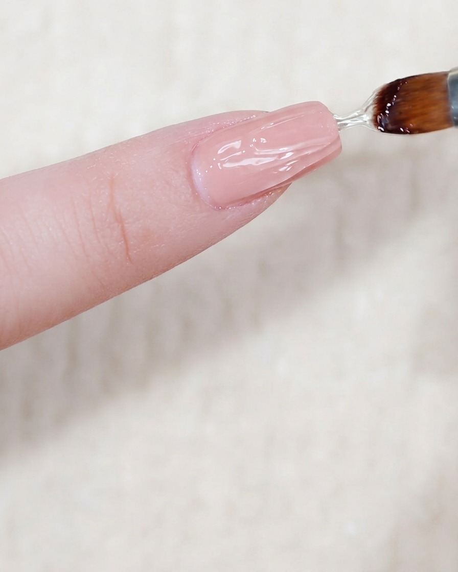 A thick, glossy layer of clear modeling gel being applied to a nail surface.
