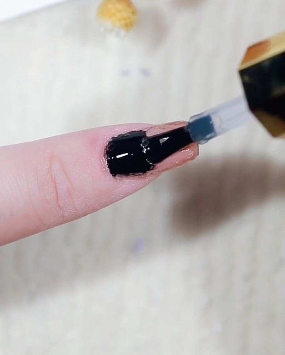 A close-up showing gold metallic powder being carefully buffed onto the raised edges of a nail using a small applicator.