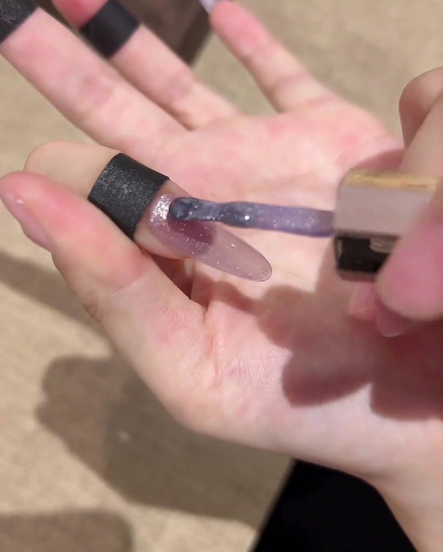 A nail brush applying a final glossy top coat over the completed galaxy cat-eye nail art.