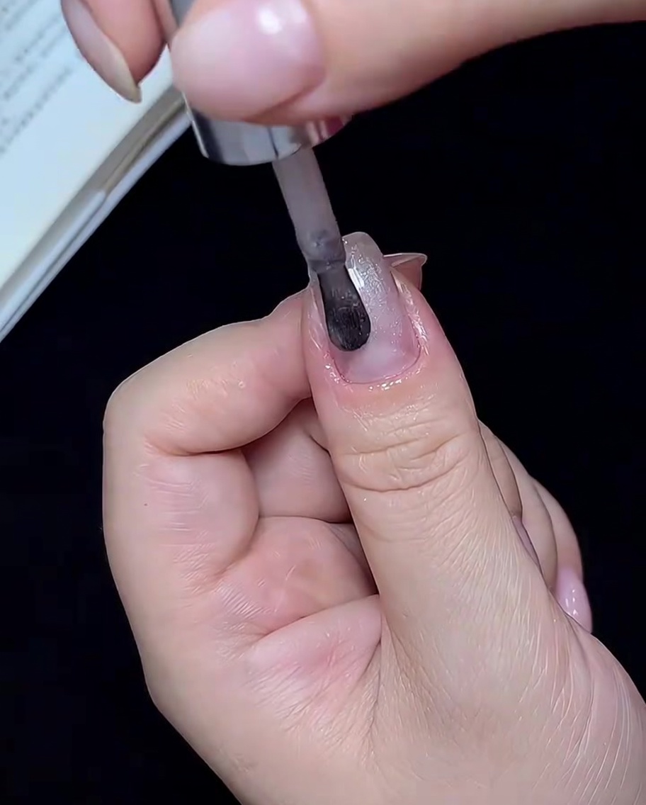 A brush applying translucent white cat-eye polish to a single fingernail.