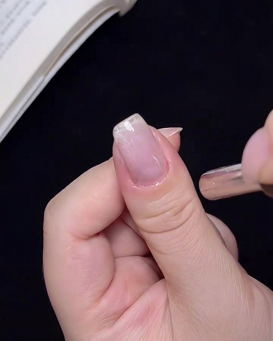 A close-up view of a metal magnet held near a nail, shifting the position of the cat-eye shimmer particles.