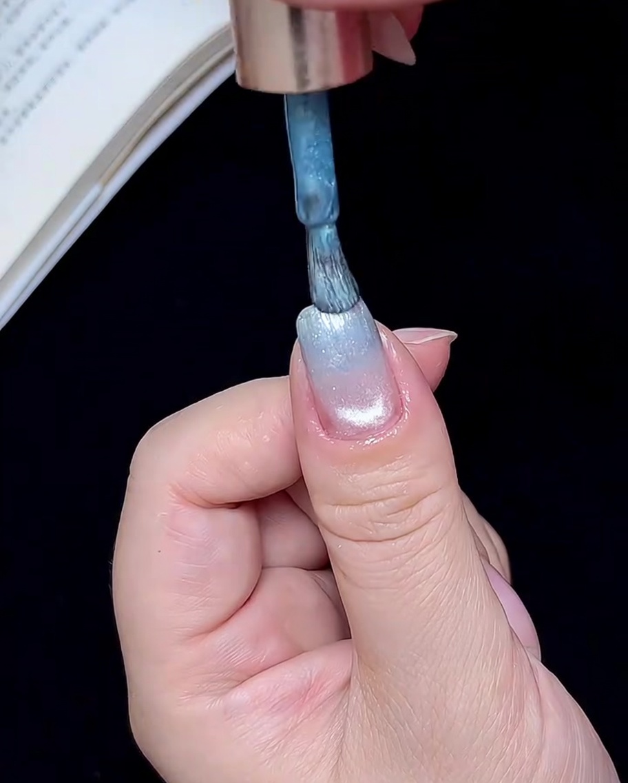 A brush applying a small amount of blue gel to the very tip of the nail.