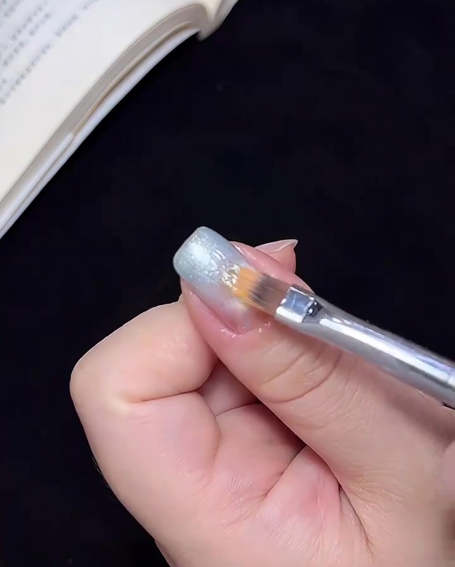 A brush blending the blue gel color toward the center of the nail to create an ombre transition.