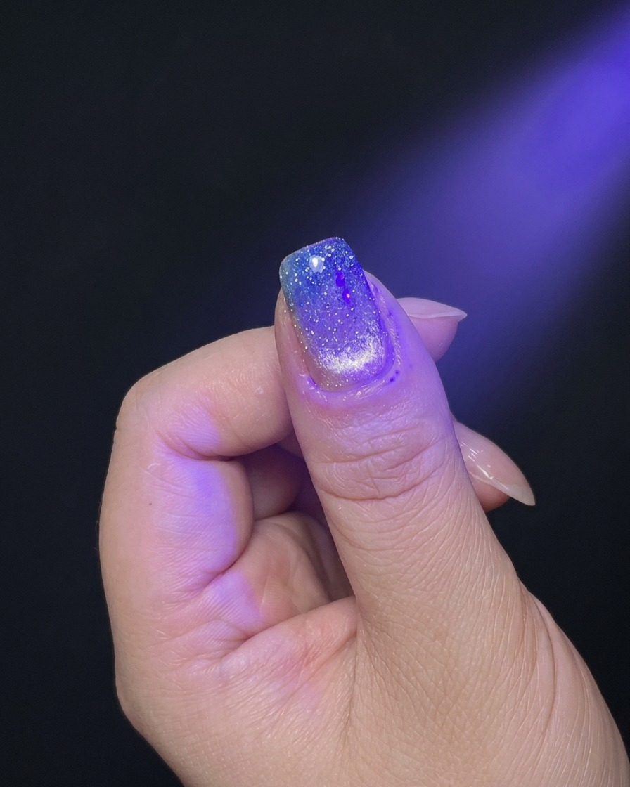 A hand positioned under the purple light of a UV/LED nail lamp for curing.
