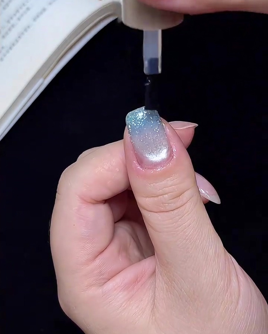 A hand inside a UV/LED lamp, with the nails being cured under the light for the final step.