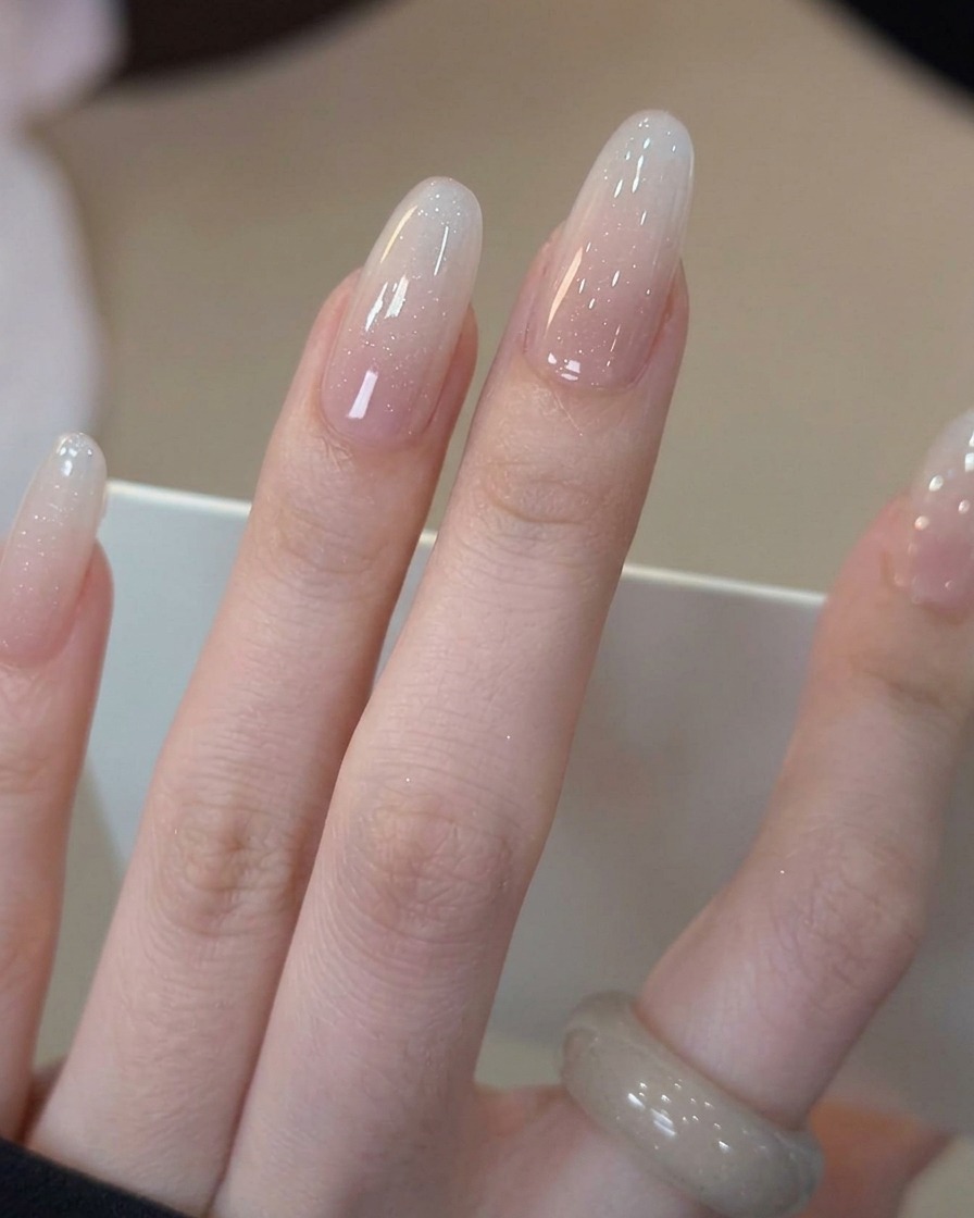A brush applying a clear, glossy top coat over the completed milky white gradient nail.