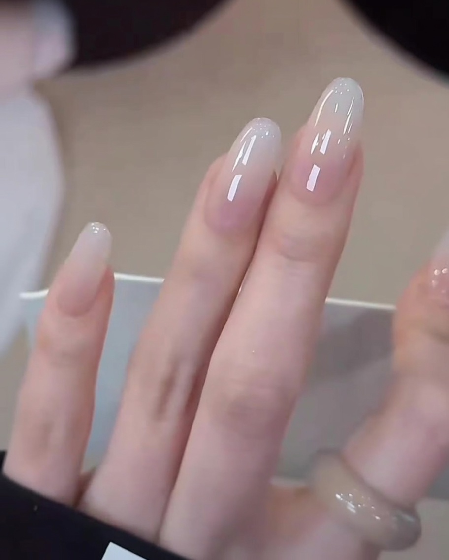 A close-up view of a hand with completed milky white gradient nails placed inside a professional UV/LED nail lamp for the final curing process.