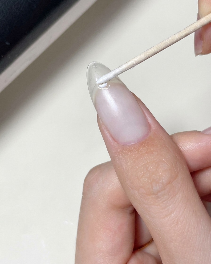 A brush applying a clear gel coat over a nail that has a star decal already placed on it.
