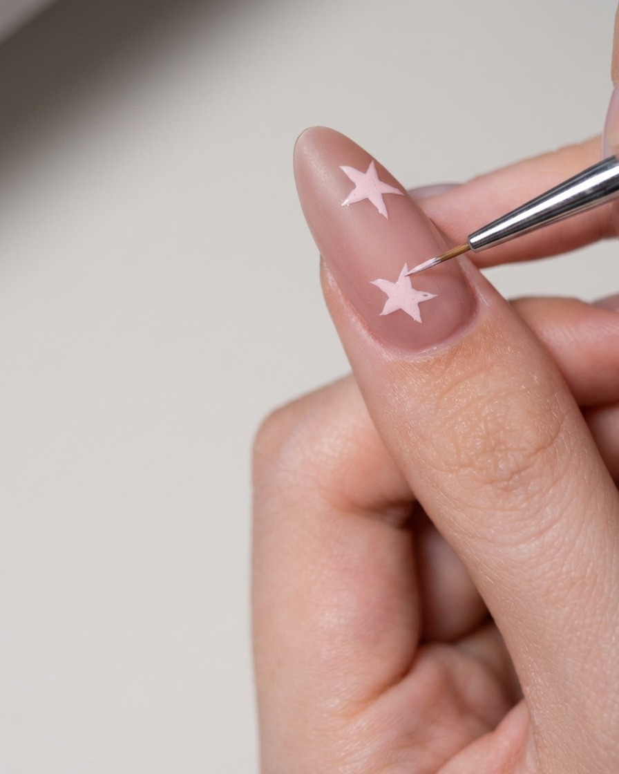 A small tool applying white nail art paste to fill in a star shape on the nail.