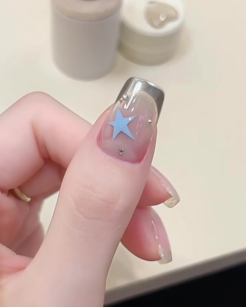 A sponge applicator applying silver chrome powder to the tip of a fingernail over a stencil.