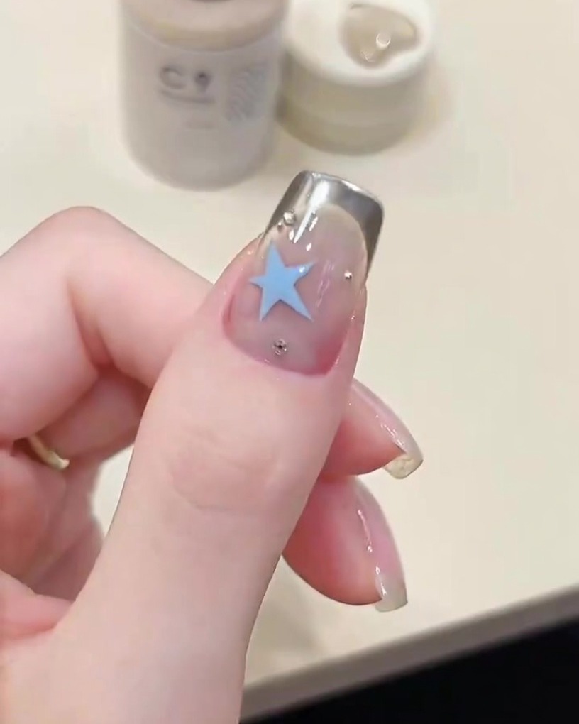 A pair of tweezers carefully lifting a French tip stencil off a fingernail, revealing a crisp silver chrome line.