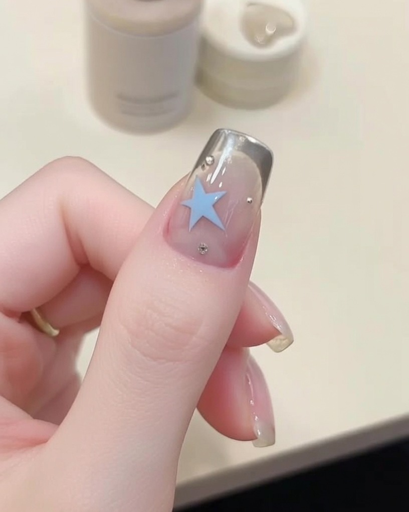 A close-up shot of a fine liner brush applying blue gel to create a star shape on a nail surface.