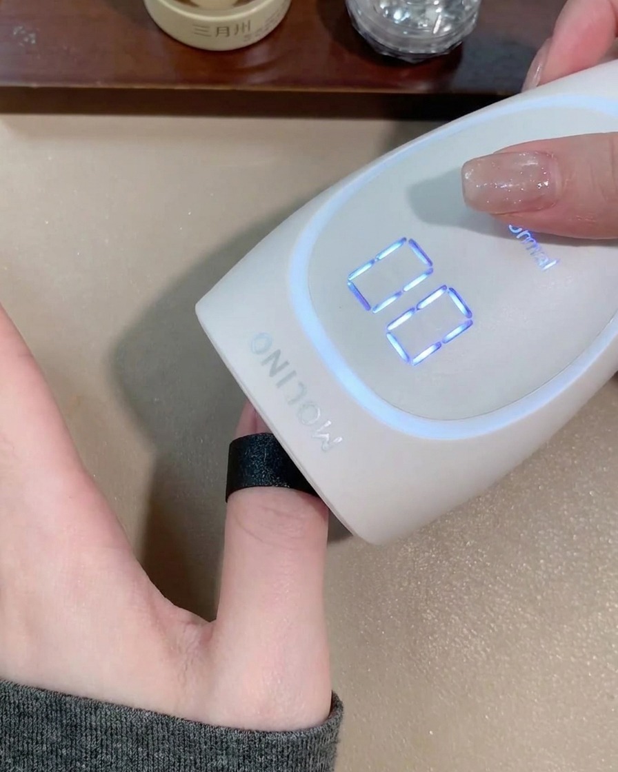 A hand positioned inside a matte white portable nail lamp to cure the cat eye gel.