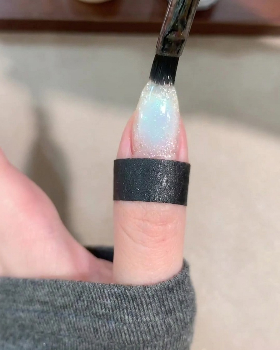 A gel brush applying a clear layer of base coat over the decorated nail.