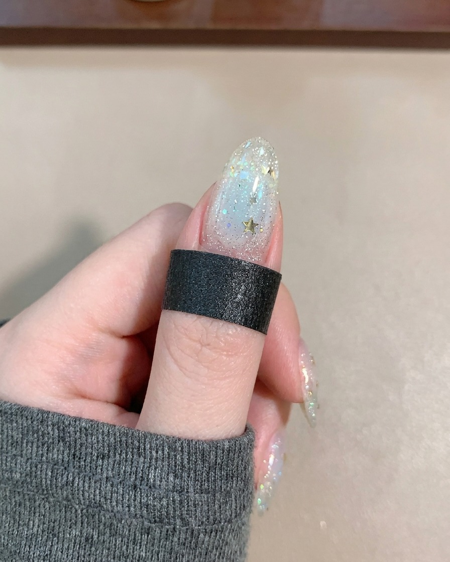 A brush applying a clear, glossy top coat over a nail decorated with star sequins and delicate lines.