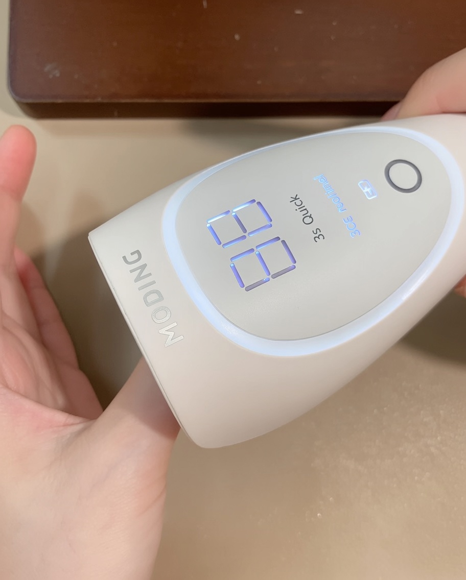 A hand placed under a portable matte white LED nail lamp, with the digital display showing the curing time.