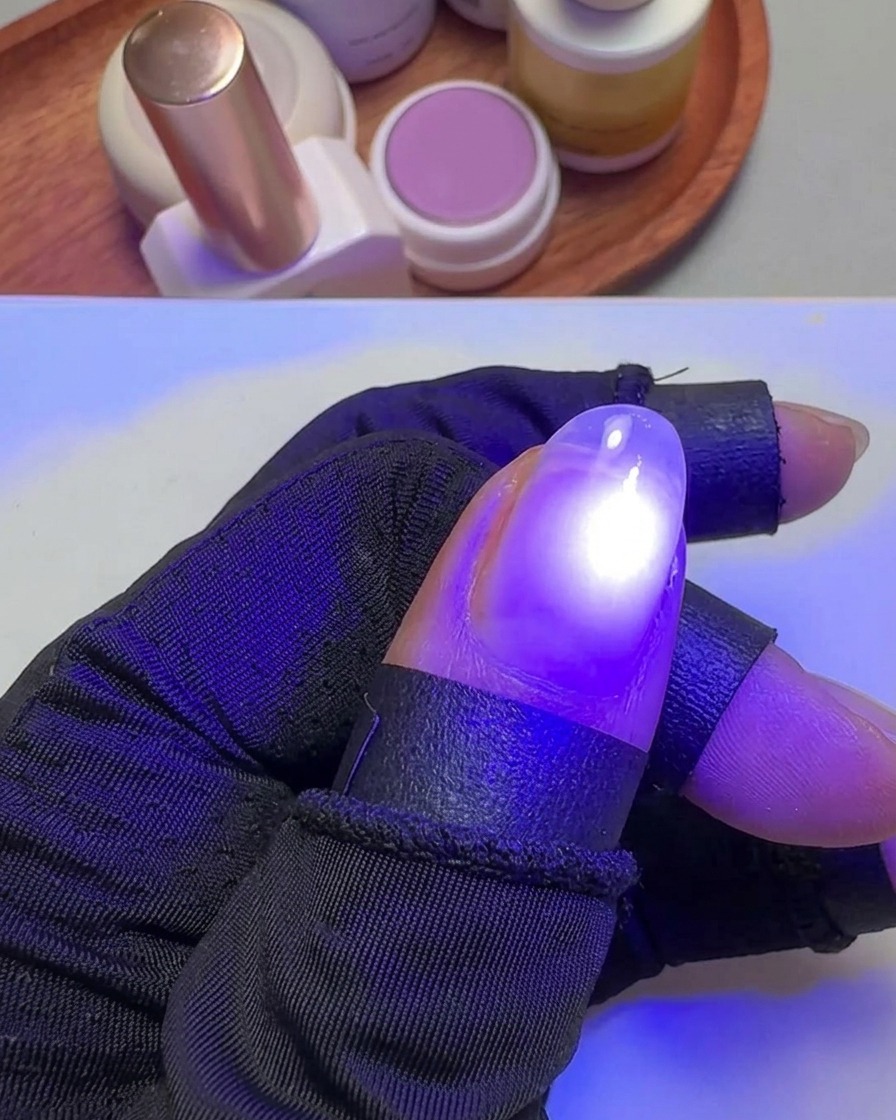A hand holding a thumb under a small, targeted purple UV light to cure the gel polish.