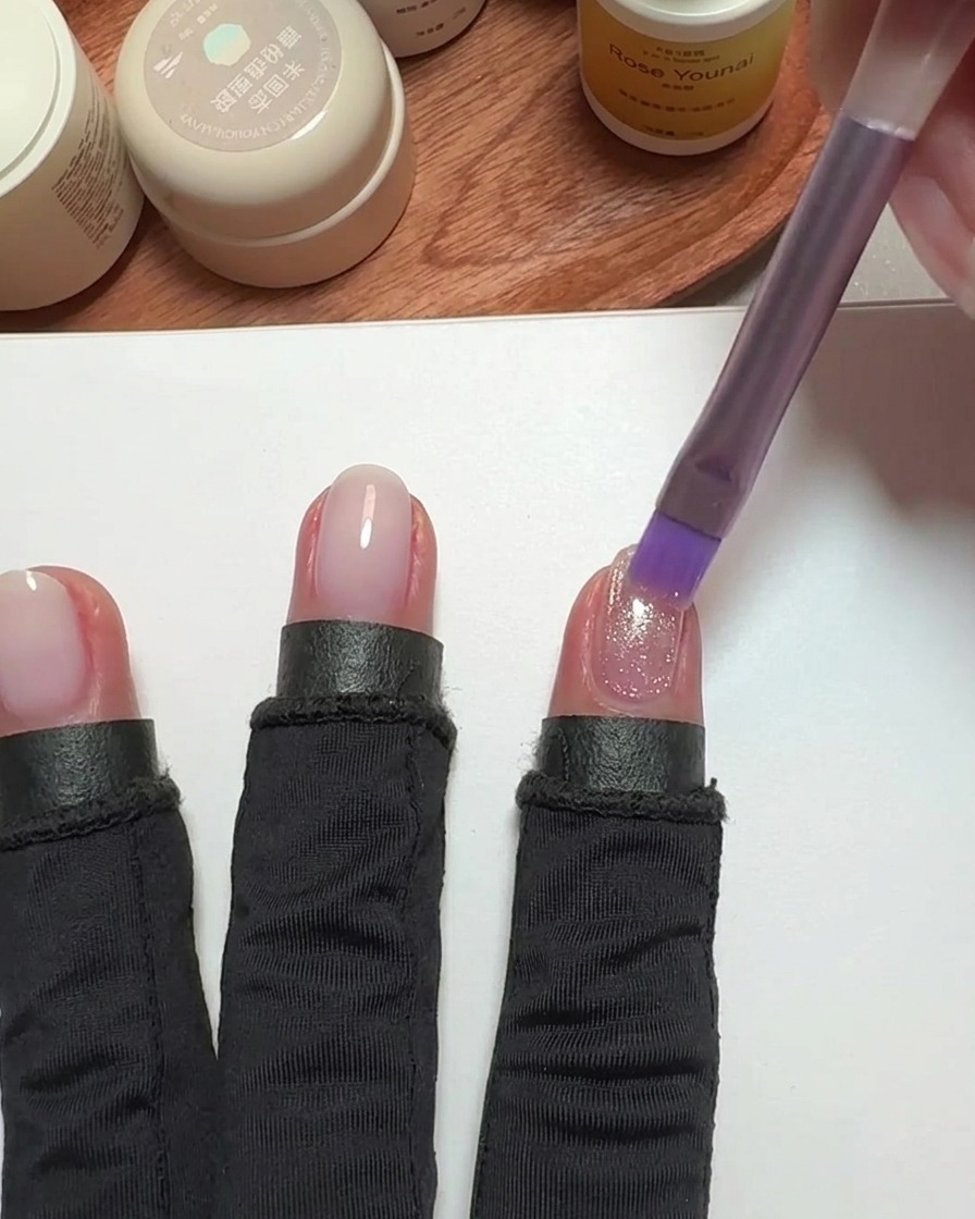 A brush applying pink cat-eye polish to a fingernail.