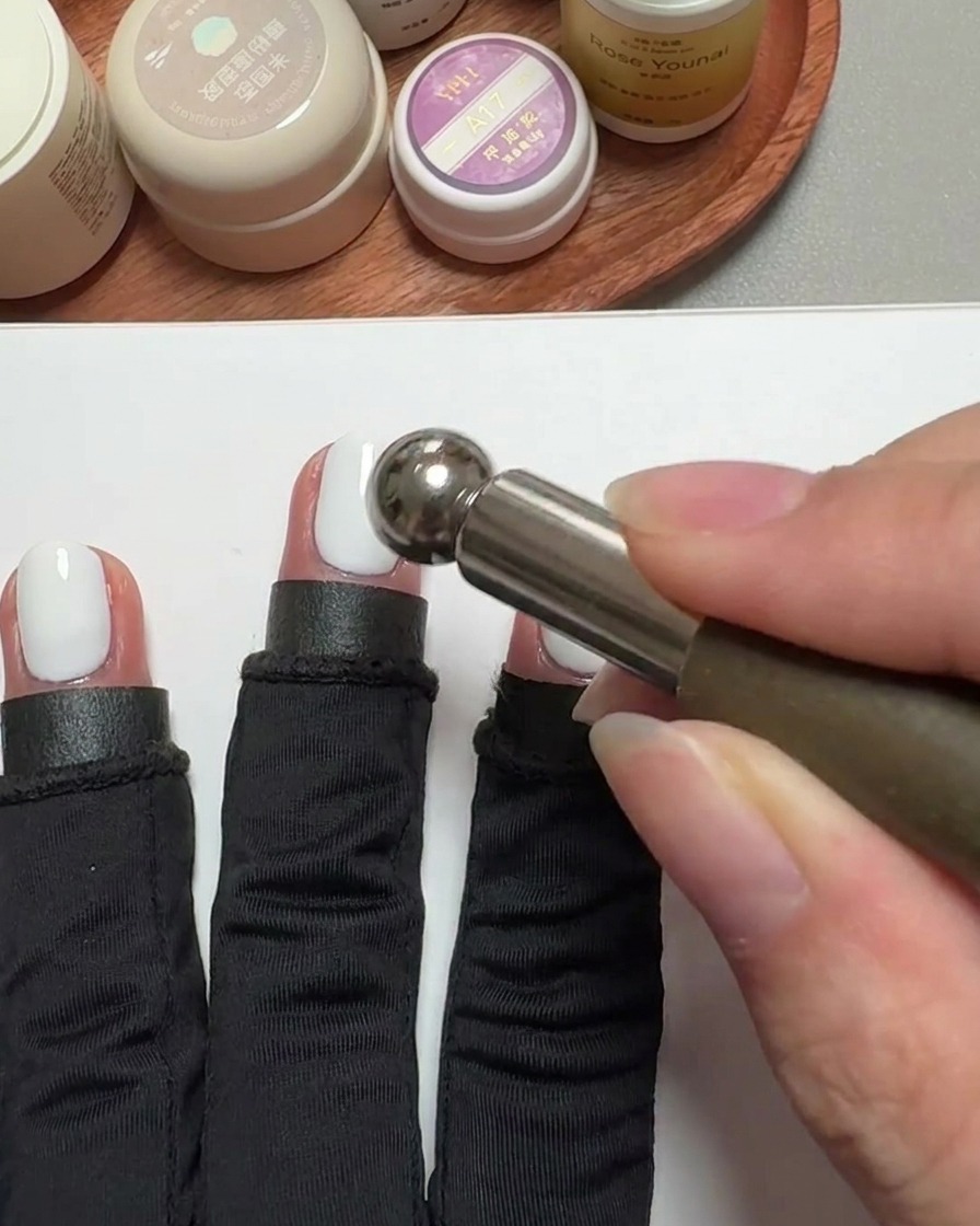A close-up of a cylindrical magnet tool hovering over a gel-coated fingernail to create a cat-eye effect.