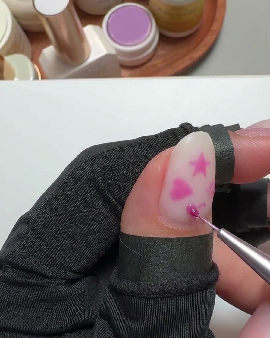 A small sticker transfer being placed over a heart-shaped design on a nail.