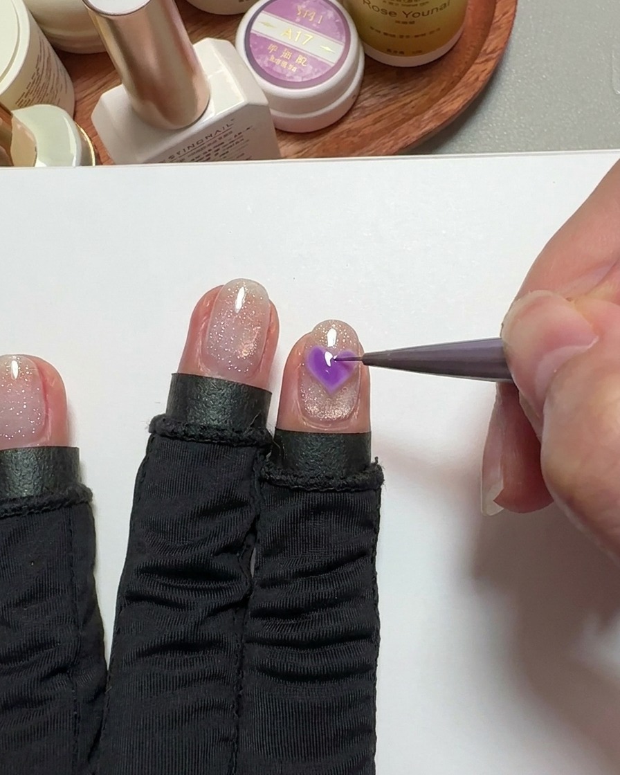 A fine-detail brush filling in a heart shape on the nail with pink gel.