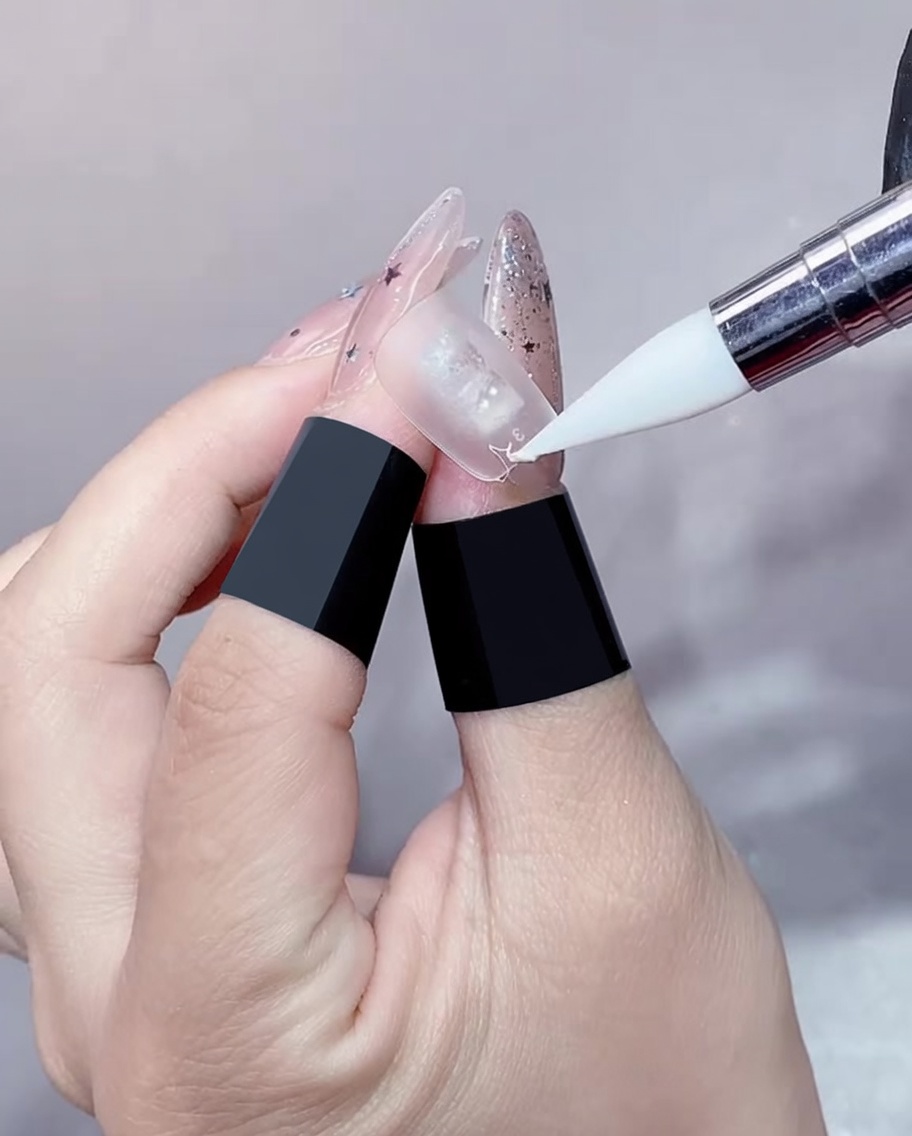 A close-up view of a gel brush applying a thin, clear gel to the edge of a nail extension.