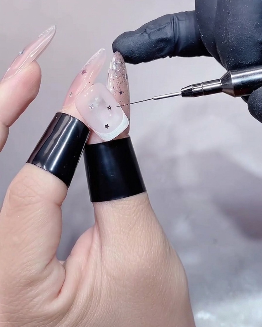 A close-up view of a hand inside a UV/LED lamp, focusing on the decorated nail with silver stars during the curing process.