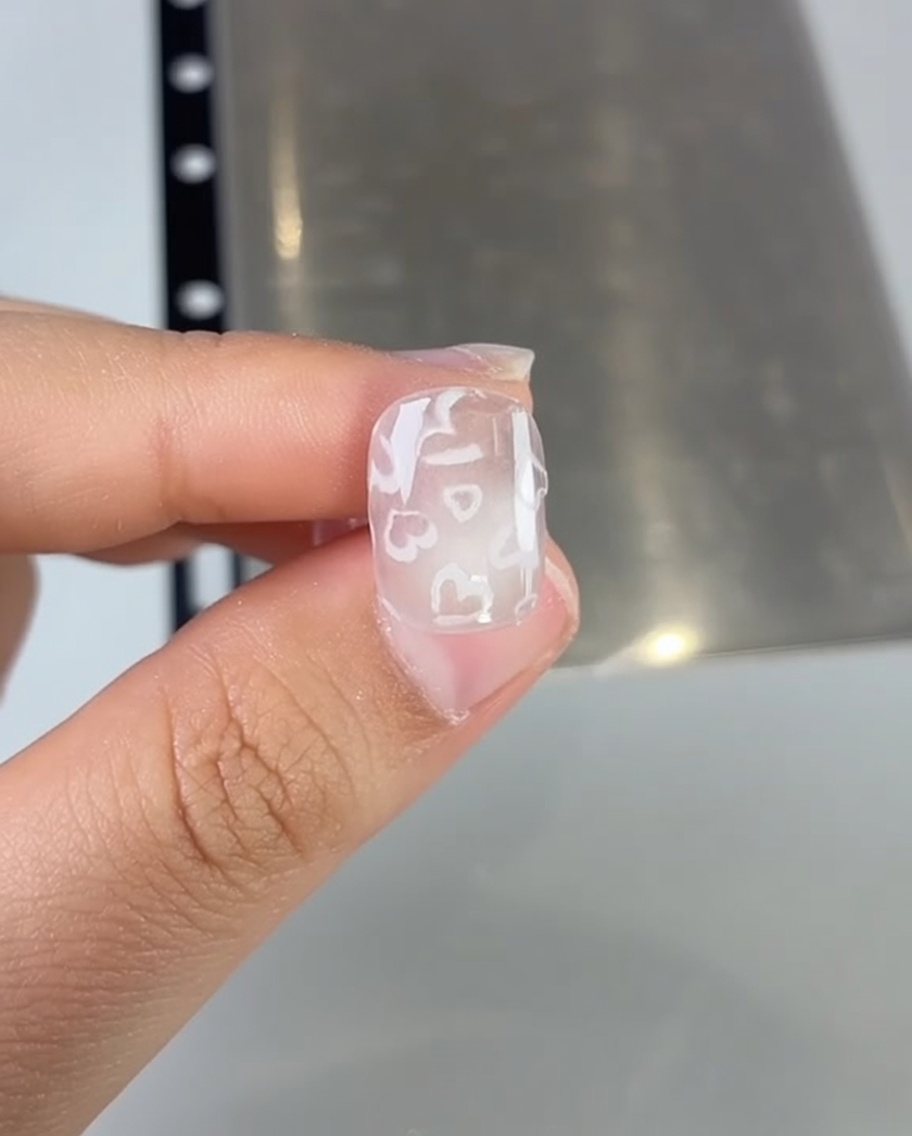 A close-up of a nail brush applying pink gel polish to a nail.