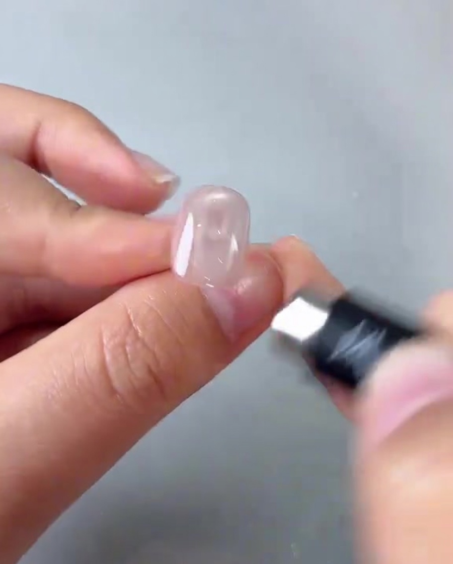 A close-up of a hand holding a small cylindrical magnet over a glossy pink nail, creating a bright circular reflection.