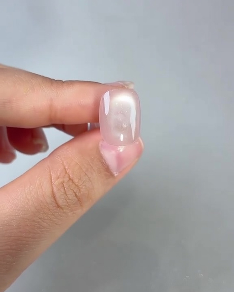 A brush applying a clear top coat to a cured pink cat-eye nail.
