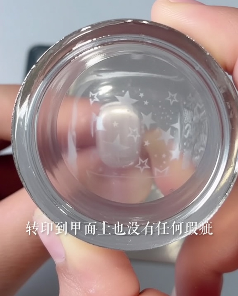 A clear stamper transferring a star pattern onto a pink nail.