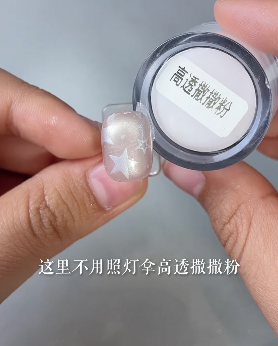 A close-up view of a fingernail with a star design being dipped into a small container of translucent powder.