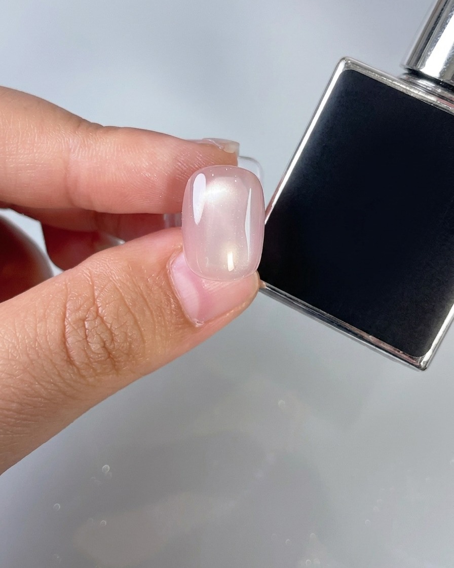 A nail brush applying a thin layer of clear top coat over a pink nail.