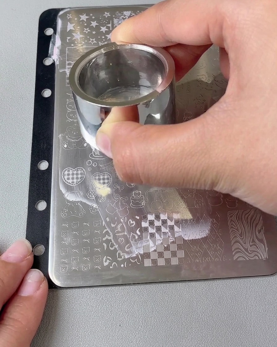 A close-up of a large stamper head holding a transferred heart design being pressed onto a nail.