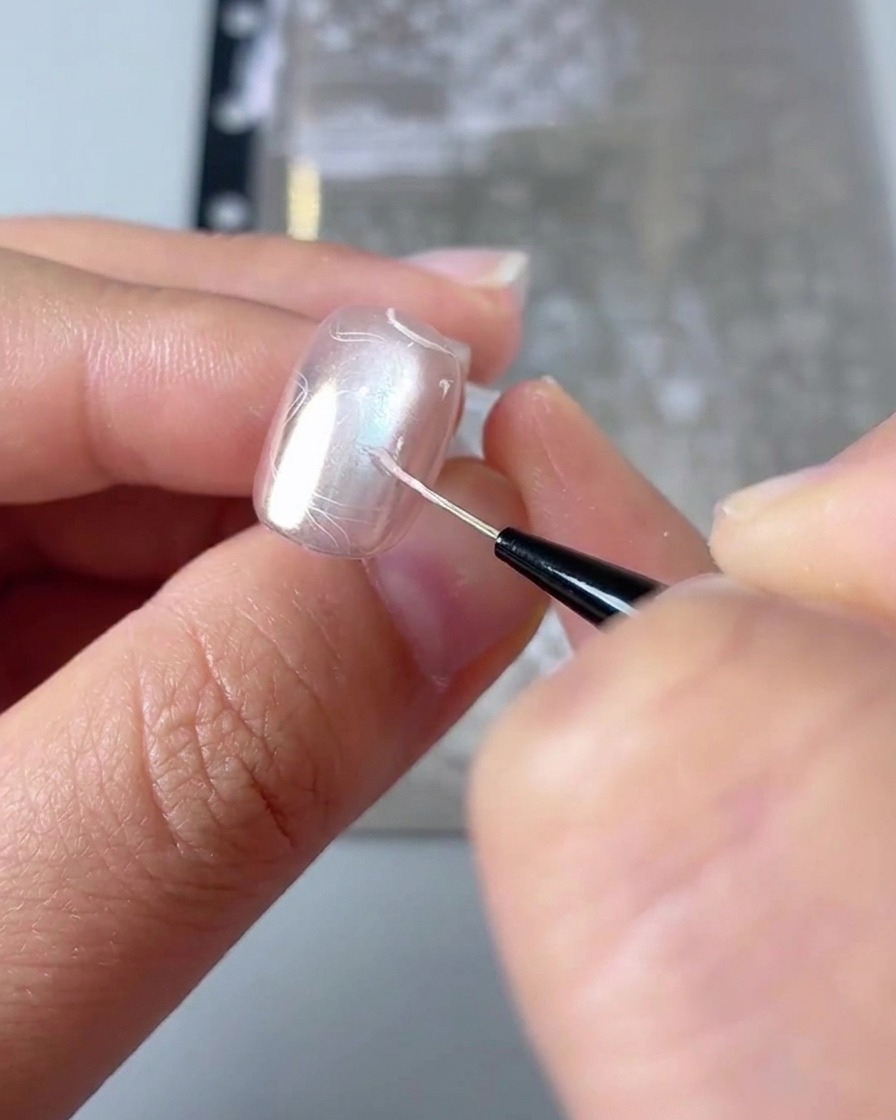 A close-up showing a fine liner brush filling in the details of a stamped heart design on a nail.