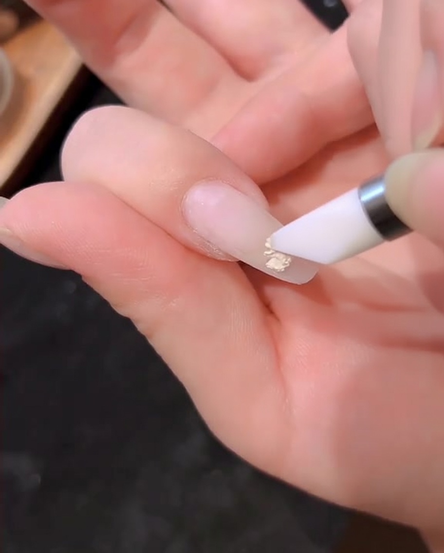 A gel polish brush applying a layer of milky white gel onto a natural fingernail.