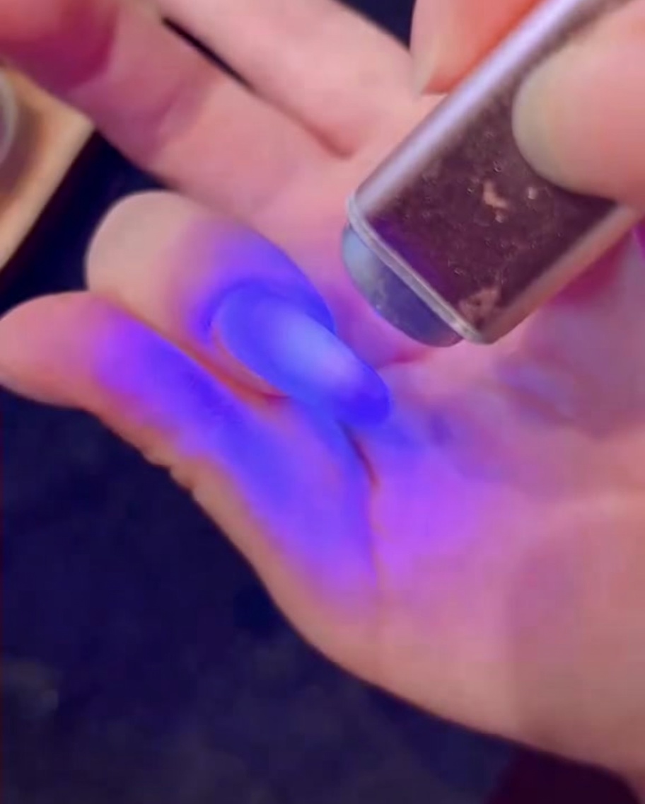 A brush applying a layer of white gel with diamond-like glitter onto a nail.