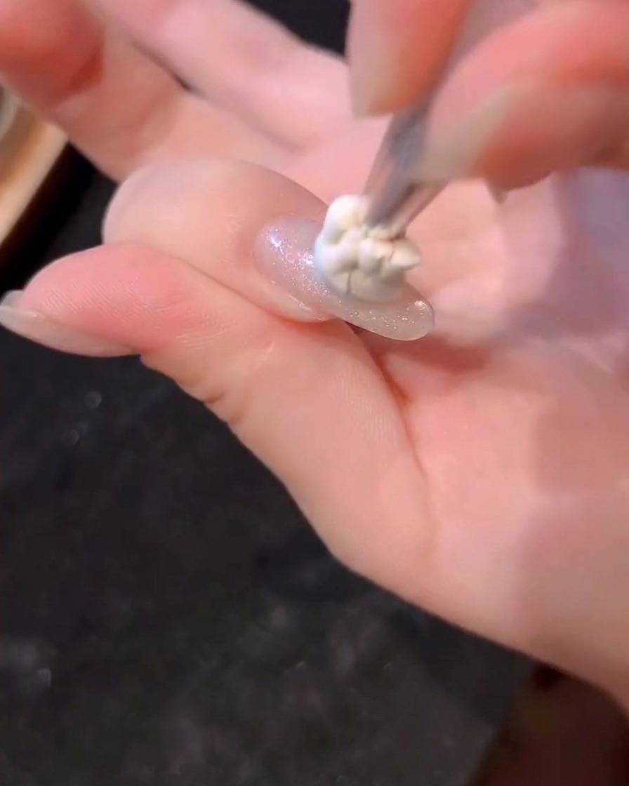 A small dot of blue gel being dabbed onto the center of a fingernail with a brush.
